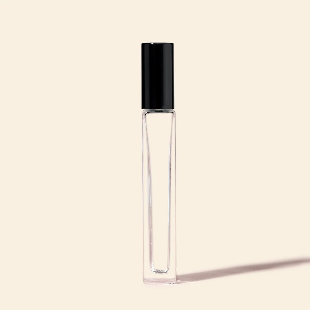A slender transparent perfume bottle with a black cap on a beige background.
