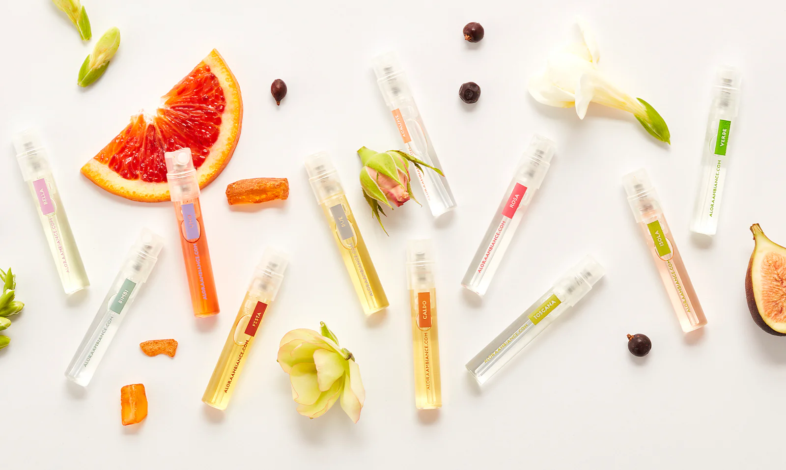 Assorted perfume sample vials with flower petals and spices on white background.