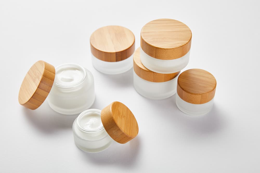 Cosmetic jars with wooden lids, white background.