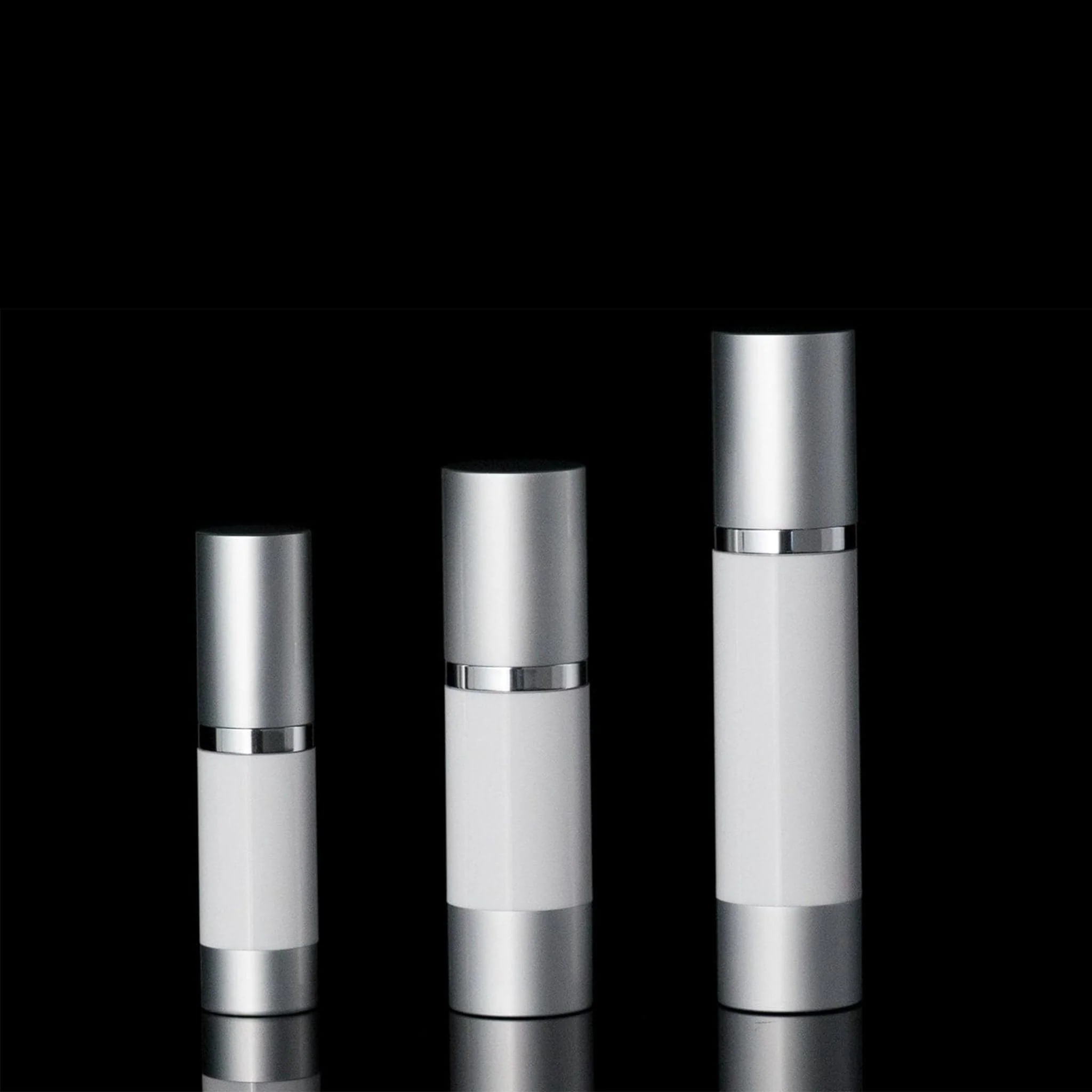 Three sleek silver and white cosmetic bottles of varying sizes on black.