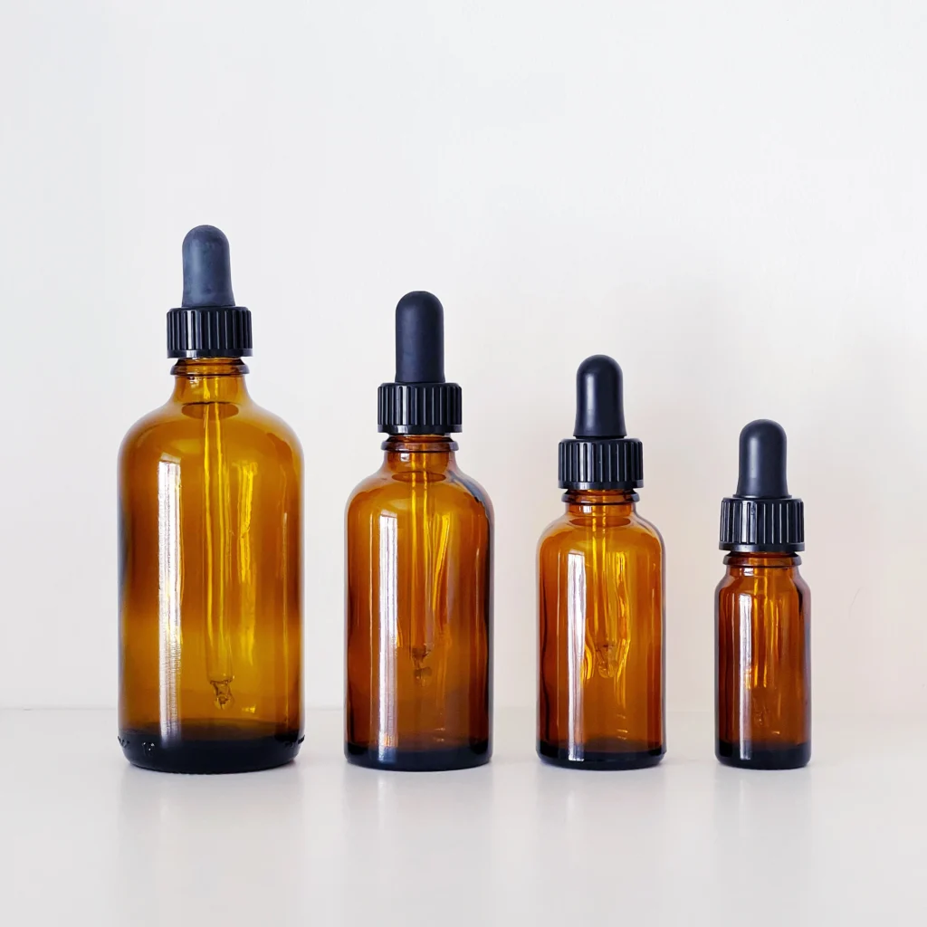 Four amber glass dropper bottles of varying sizes against a white background.