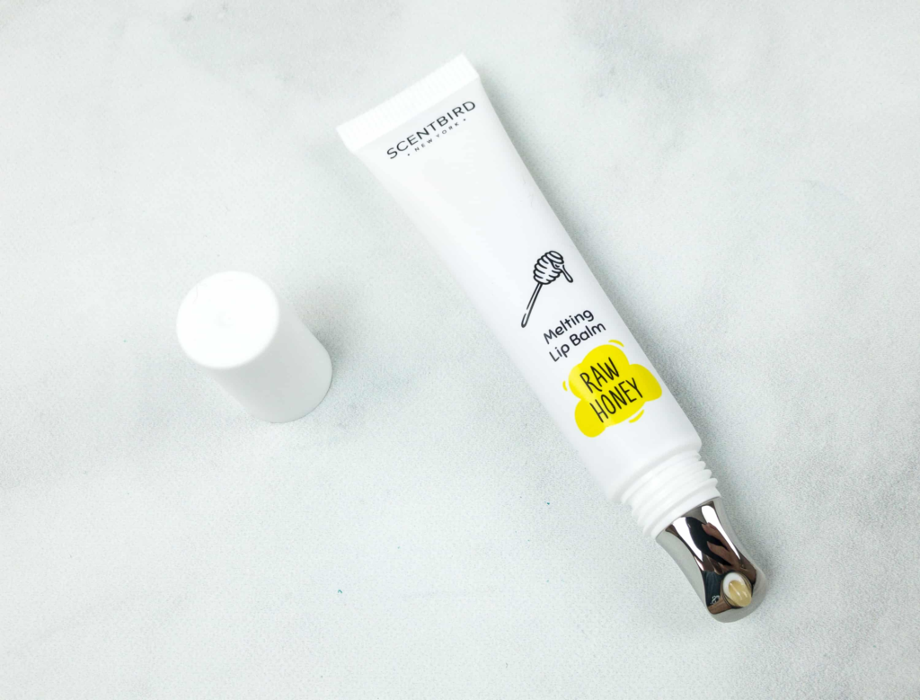 A white cosmetic tube with a black applicator on a marble surface.